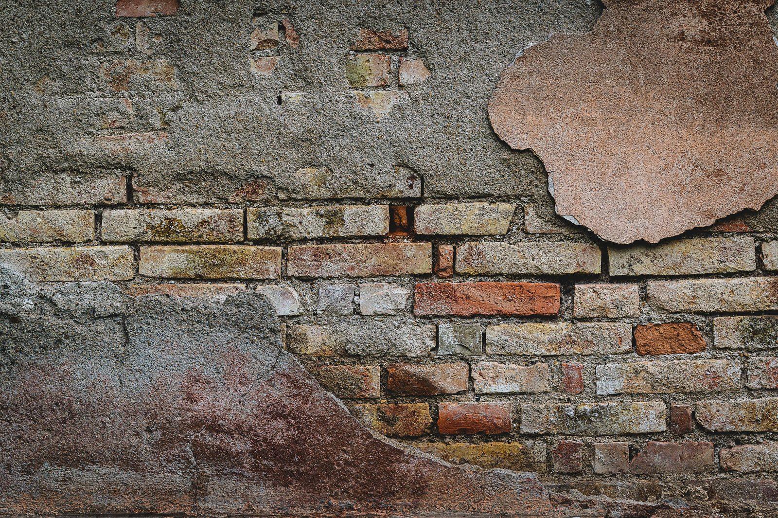 A masonry wall with failed stucco render exposing the brickwork and mortar joints beneath