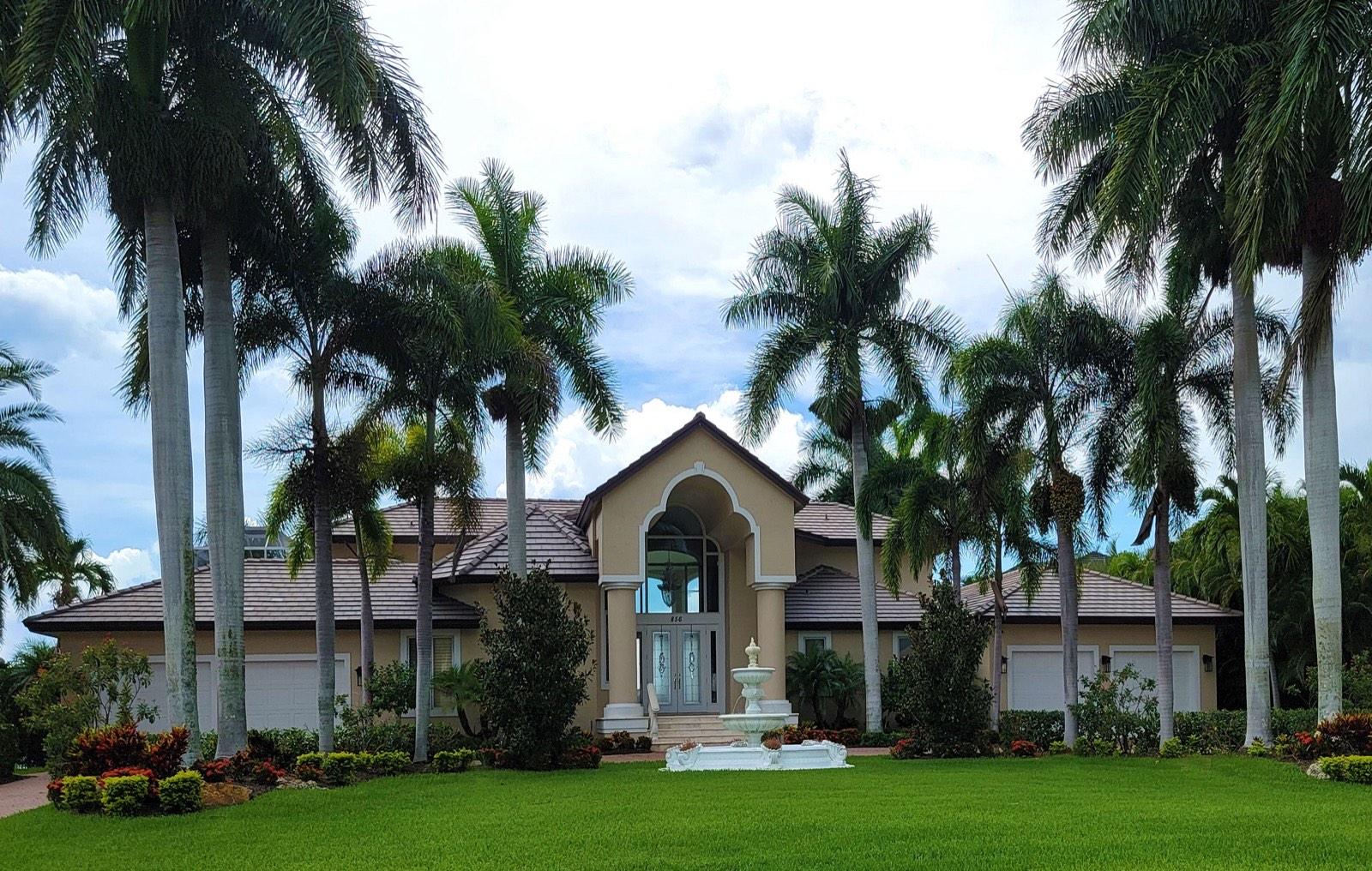 A Florida home with a tile roof, royal palms and a fountain in the front lawn