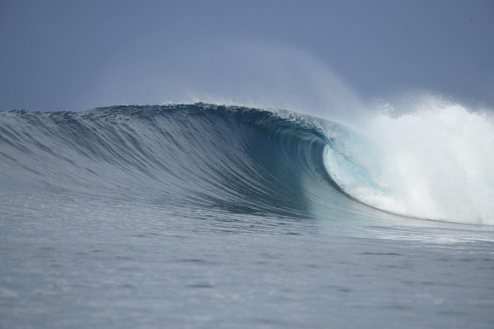 A breaking ocean wave curling into a barrel under a clear sky